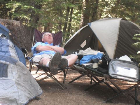 1991 Ford Bronco - A man rests in a camping chair at a campsite, surrounded by tents and trees.