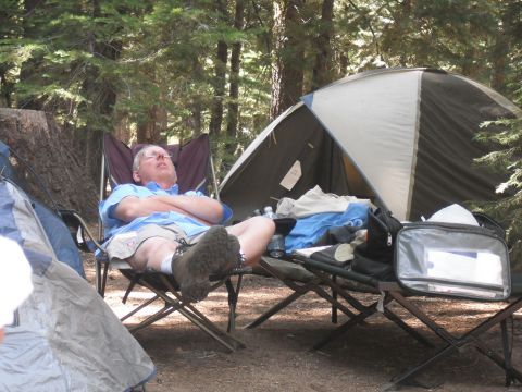 1991 Ford Bronco - A man rests in a camping chair at a campsite, surrounded by trees and camping gear.