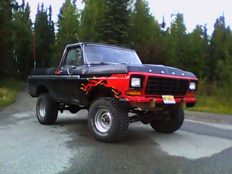 1978 Ford Bronco - Three-quarter front view of a lifted black late-1970s Ford Bronco with a red front clip, black hood with FORD lettering, and orange-yellow…