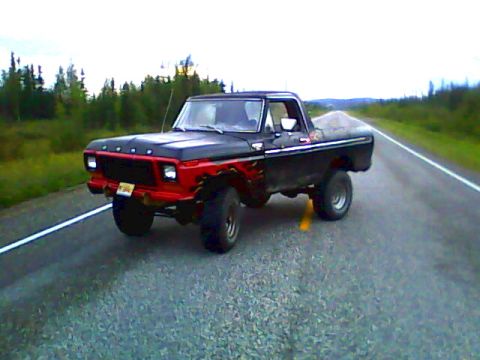1978 Ford Bronco - Lifted black late-1970s Ford Bronco with a red front clip and flame graphics, photographed at a three-quarter front angle on an open two-la…