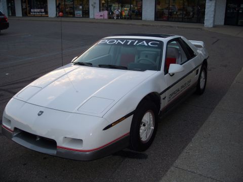 1971 Ford Ranchero - A white Pontiac Fiero is parked on a street in front of a strip mall.