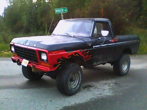 1978 Ford Bronco - Three-quarter front view of a lifted late-1970s Ford 4x4 in flat black with a red front clip and orange/yellow flame graphics along the fen…