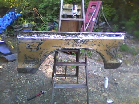 1978 Ford Bronco - A removed front fender propped on a metal stool outdoors, stripped to bare metal and coated in patches of tan body filler with dark old pai…