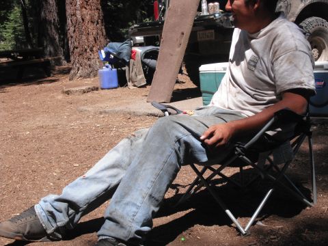 1991 Ford Bronco - A man relaxes in a camping chair at a campsite, with a truck and cooler visible behind him.