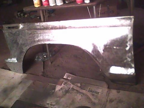 1978 Ford Bronco - A front fender stripped to bare metal and sanded, propped upright on a shop floor in front of a workbench lined with spray cans. Grinding s…