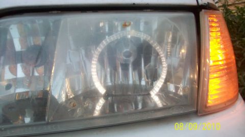 2004 Ford Crown Victoria - Close-up of a car's front lighting assembly, showing a hazed headlight with a halo ring and an illuminated amber turn signal.