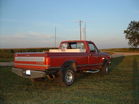 1988 Ford F-150 - This red 1988 Ford F-150 pickup truck is parked on a grassy area with a cornfield behind it.