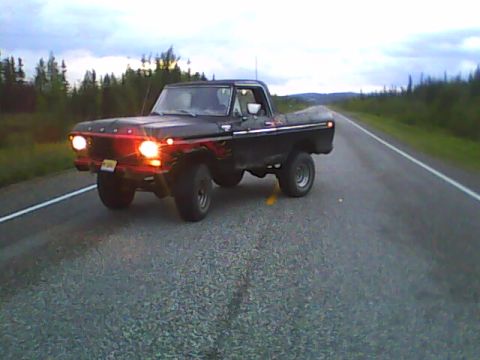 1978 Ford Bronco - A black Ford pickup truck drives down a highway with a cloudy sky overhead.