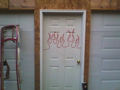 1978 Ford Bronco - A white six-panel shop entry door framed in bare OSB between two white garage doors, with a red pinstriped flame outline laid out on it as…