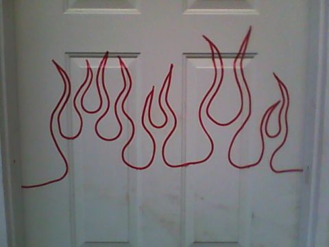 1978 Ford Bronco - A red flame outline laid out in thin pinstripe tape on a white paneled interior door, marking out the licks before painting. No vehicle is…