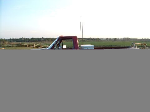 1988 Ford F-150 - A red pickup truck is parked in a grassy field with a wooden fence in the background.