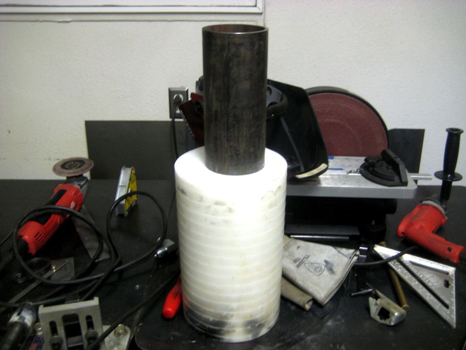 Metal pipe on top of stacked white discs, with tools like grinders and a sander in the background