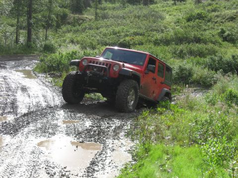 1990 Ford F-250 - Red Jeep Wrangler navigating a challenging muddy off-road trail.