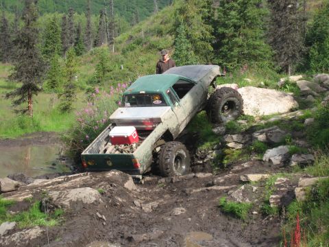1990 Ford F-250 - A heavily modified pickup truck navigates a challenging off-road course with a person standing nearby.