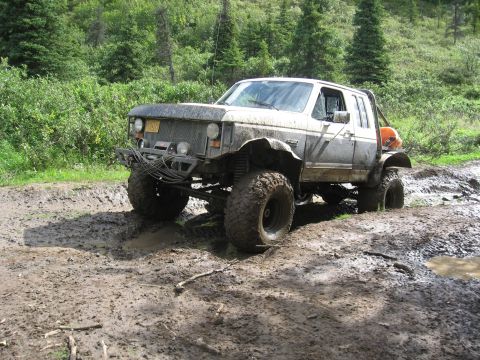 1990 Ford F-250 - Heavily modified pickup truck navigating a challenging muddy off-road course.