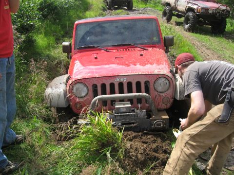 1990 Ford F-250 - A red Jeep is stuck in the mud while people work to free it, with another vehicle in the background.