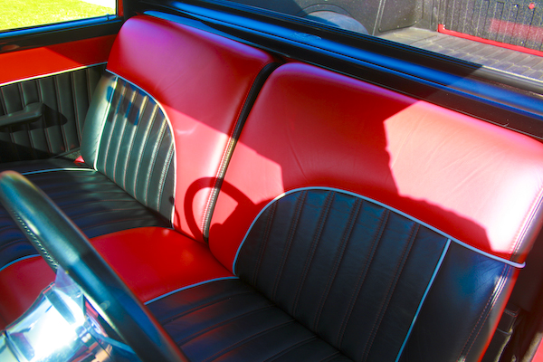 Red and black vinyl bench seat interior with chrome trim and a partial steering wheel visible