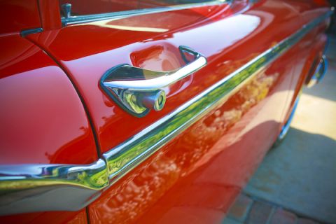 1959 Ford Ranchero - The shiny chrome door handle and trim on a red classic car reflect the surrounding environment.