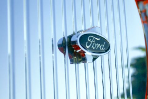 1959 Ford Ranchero - A close-up of a Ford emblem on a shiny chrome grille with vertical bars.