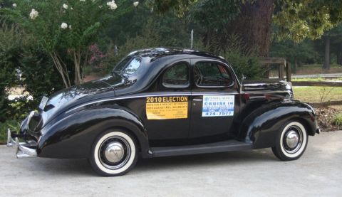 1976 Ford Ranchero - A classic black Ford Coupe from 1939 is shown from the side, whitewall tires and political and event stickers.
