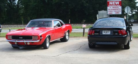 1976 Ford Ranchero - A red 1969 Chevrolet Camaro SS is parked next to a black Ford Mustang, with a "New Technology" sign in the background.