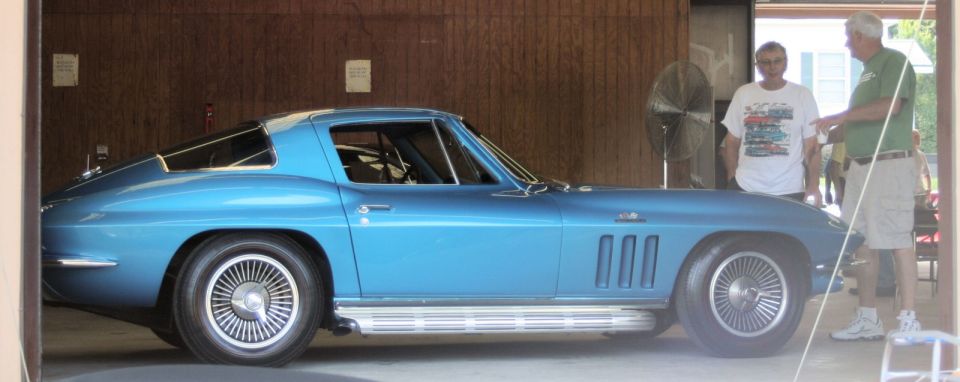 Blue 1960s Corvette Sting Ray coupe in profile inside a garage with side pipes and turbine wheels