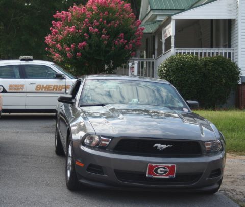 1976 Ford Ranchero - A gray Ford Mustang with a Georgia Bulldogs license plate is parked in front of a house, with a Monroe County Sheriff's vehicle nearby.