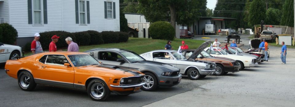 Orange 1970 Ford Mustang in foreground, followed by several other Ford Mustangs