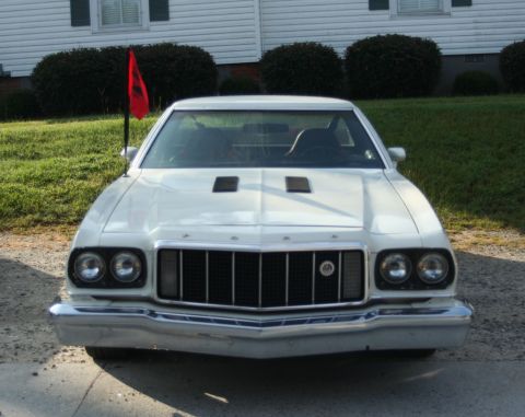 1976 Ford Ranchero - Front view of a white 1976 Ford Ranchero, distinguished by its grille and headlight design, with a red flag mounted on the driver's side fe…