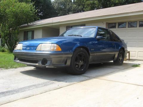 1989 Ford Mustang - A blue 1989 Ford Mustang with black wheels sits in a driveway.