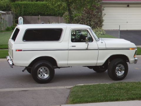 1978 Ford Bronco - A white 1978 Ford Bronco is shown from the side, parked on a street with a garage in the background.