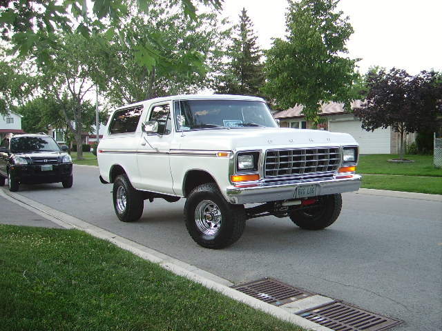 White 1978 Ford Bronco with chrome wheels and a chrome grille, seen from a 3/4 front angle on a residential street