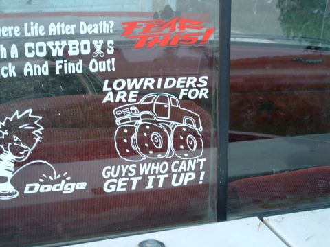 1988 Ford F-150 - Stickers on a truck window, including one depicting a monster truck and another with a cartoon character urinating on the word 'Dodge'.