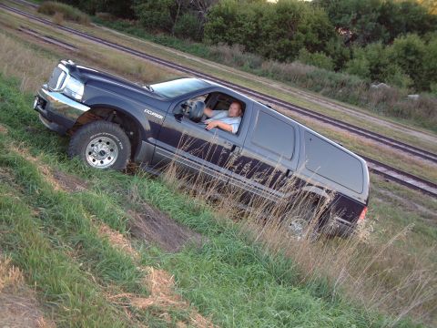 1986 Ford Bronco - Ford Excursion SUV is driven off-road near train tracks on a grassy slope.