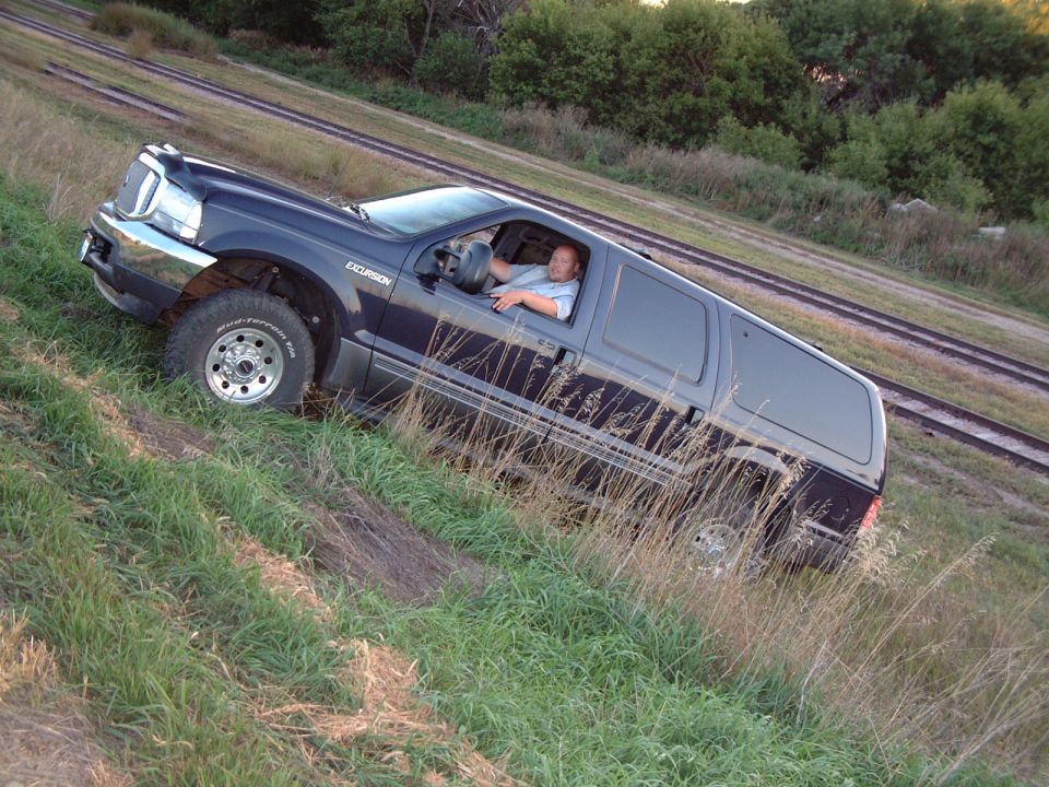 Dark blue Ford Excursion SUV driving off-road near train tracks