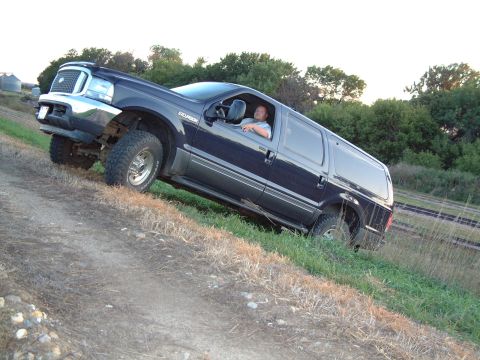 1986 Ford Bronco - This large SUV is driving off-road on a grassy slope, with a driver behind the wheel.