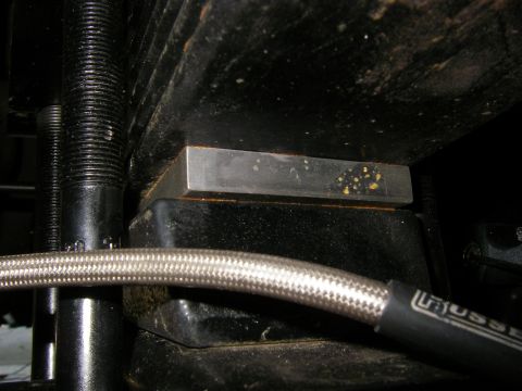1990 Ford Bronco - Close-up view of a metal block on a suspension component, with a braided hose in the foreground.