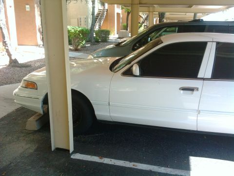 1997 Ford Crown Victoria - A white 1997 Ford Crown Victoria is parked under a carport, with another vehicle visible behind it.