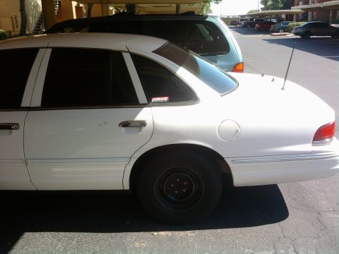 1997 Ford Crown Victoria - A white 1997 Ford Crown Victoria sedan is parked in a lot, partially covered by a carport.