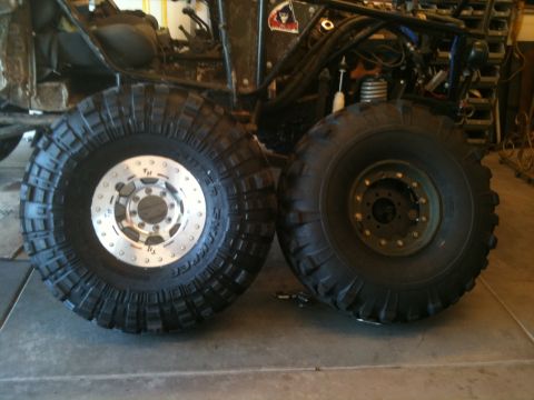 1966 Ford Bronco - A close-up view of two large off-road tires, one with a custom silver rim, positioned in front of a vehicle's frame.