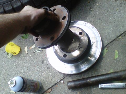 1995 Ford Bronco - A hand holds a brake rotor and hub assembly next to a can of PB Blaster and a metal rod on a concrete surface.