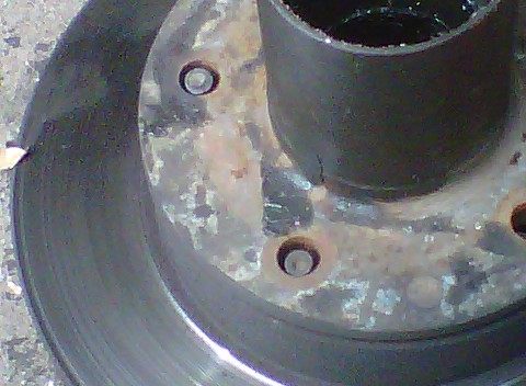 1995 Ford Bronco - Close-up of a rusty wheel hub flange and brake rotor with every wheel stud removed, leaving bare empty stud holes ringed by corrosion. The…