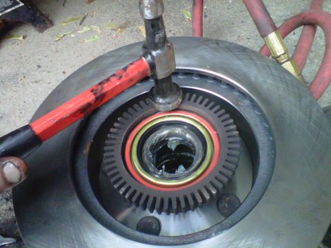 1995 Ford Bronco - A red-handled hammer and punch are used to drive a toothed ABS tone ring onto a wheel hub still attached to its brake rotor, with the orang…