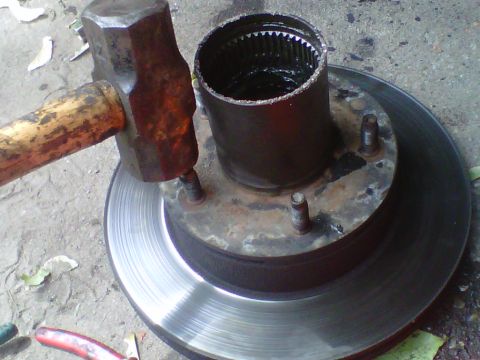 1995 Ford Bronco - A rusty front hub and brake rotor assembly lying face-up on concrete, with the internally splined locking-hub barrel visible in the center…