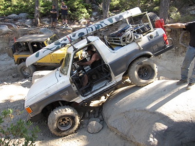 1991 Ford Bronco - Modified 1991 Ford Bronco tackling a difficult off-road obstacle, with another vehicle in the background.