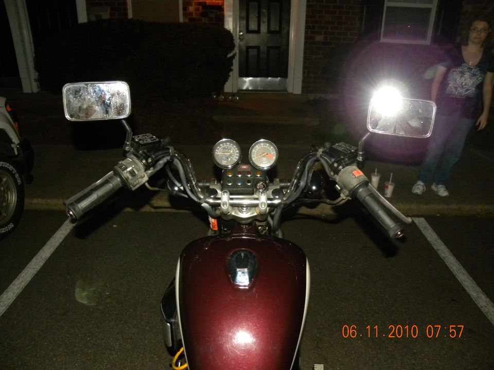 Maroon motorcycle fuel tank and handlebars with dual gauges. A person stands in the background