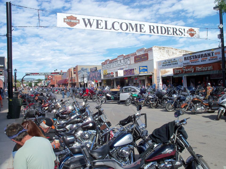 Motorcycles packed along a rally main street under a Harley Welcome Riders banner