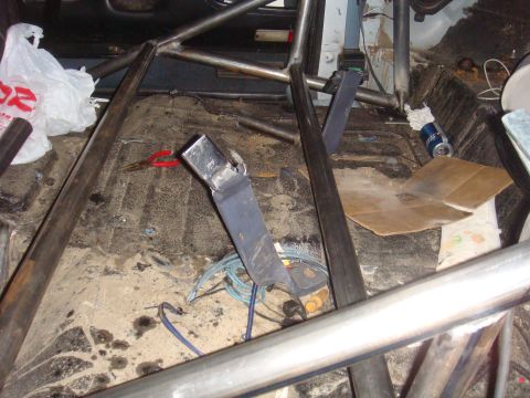 1992 Ford Bronco - The interior of a vehicle shows a roll cage, a seatbelt buckle, and various debris scattered on the floor.
