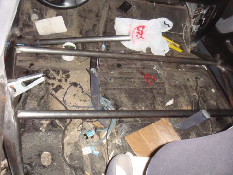 1992 Ford Bronco - The interior of a vehicle shows a custom roll cage with tools and debris scattered on the floor.