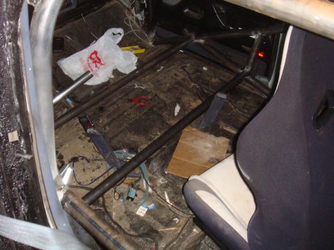 1992 Ford Bronco - Vehicle interior with a roll cage and racing seat, showing debris and wiring on the floor.